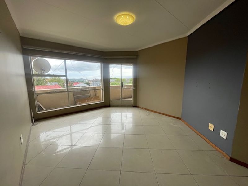An empty, open-plan living area featuring large windows, tiled flooring, and direct access to an outdoor balcony space.