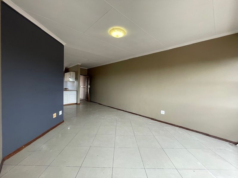 An empty open-plan living area featuring tiled flooring and neutral wall finishes, with a view through to the kitchen area.