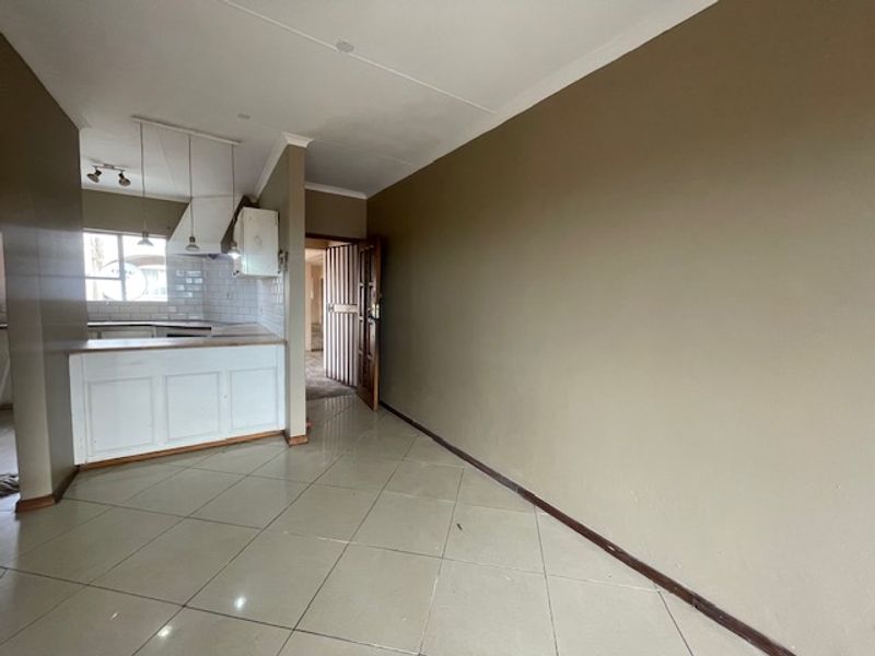 An open-plan living and kitchen area featuring tiled flooring, a breakfast counter, and built-in kitchen cabinetry, presenting a blank canvas for renovation.