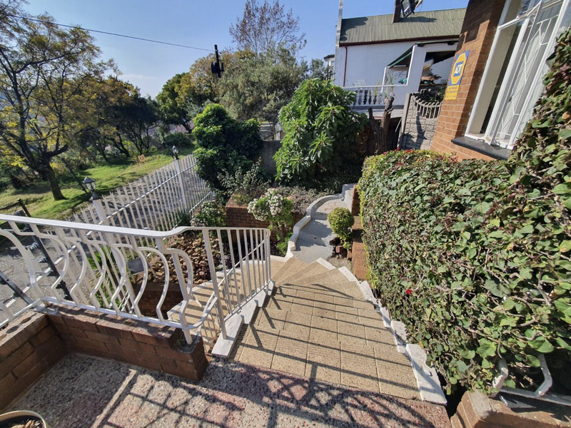 Exterior view of a brick staircase leading to the property entrance, featuring metal railings and established garden landscaping.