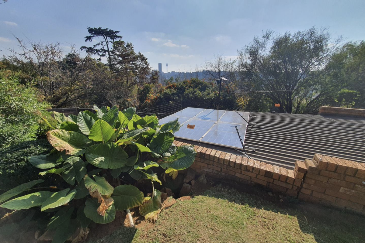 Rear view of the property featuring a corrugated metal roof with installed solar panels, a brick retaining wall, and an electric fence.