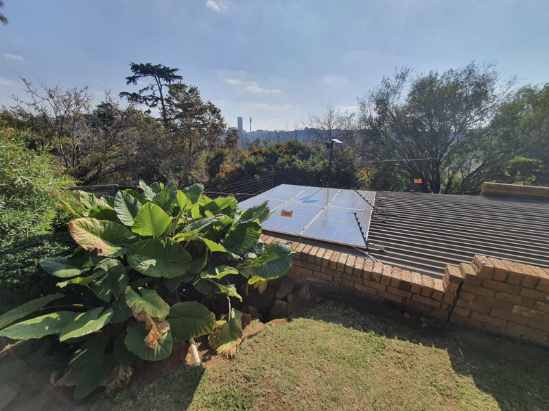 Rear view of the property featuring a corrugated metal roof with installed solar panels, a brick retaining wall, and an electric fence.