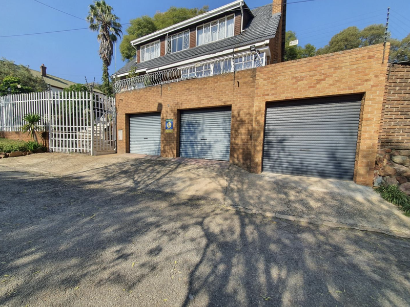 Front elevation of a multi-story house featuring a triple garage with roller shutter doors, brick facade, and secure perimeter fencing.