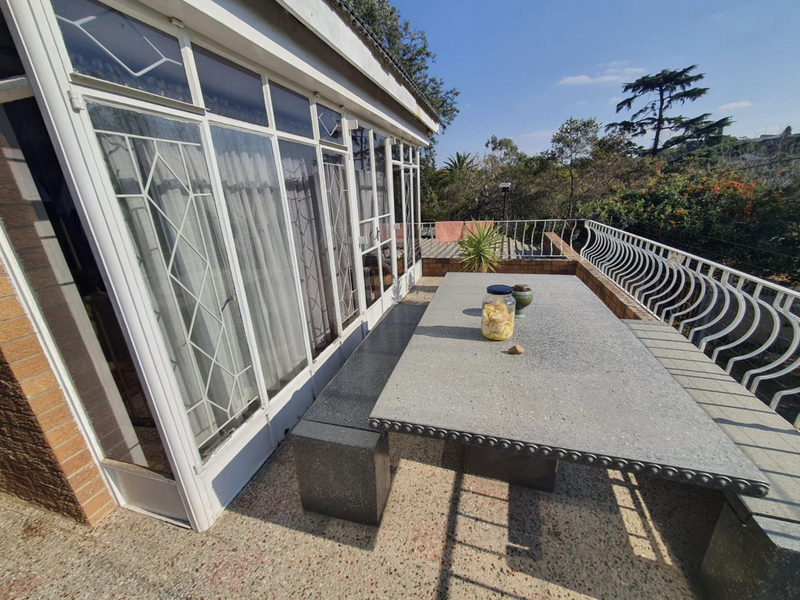 Spacious outdoor balcony featuring terrazzo flooring, a built-in stone dining table, and large glass sliding doors providing access to the interior.