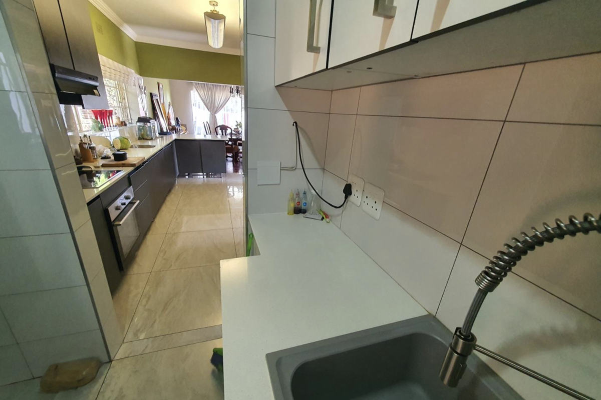 Modern kitchen featuring sleek cabinetry, stone countertops, tiled backsplash, and high-quality fixtures, flowing into an open-plan living and dining area.
