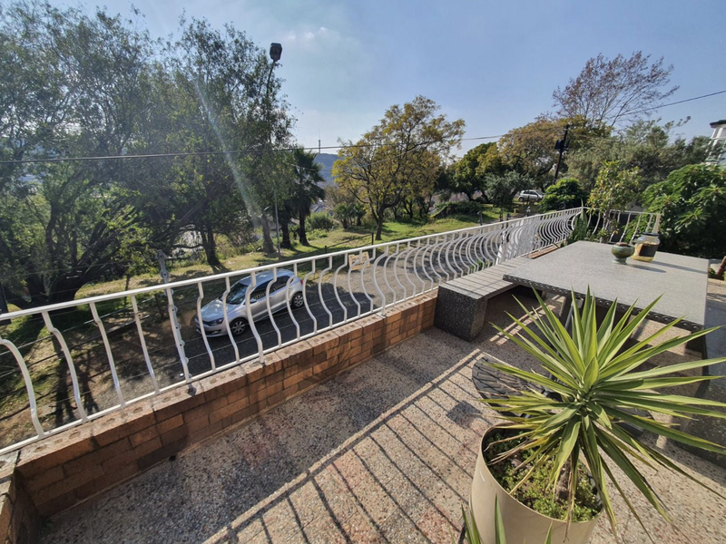 An elevated outdoor balcony featuring a brick and metal balustrade, offering an open view of the surrounding garden and driveway area.