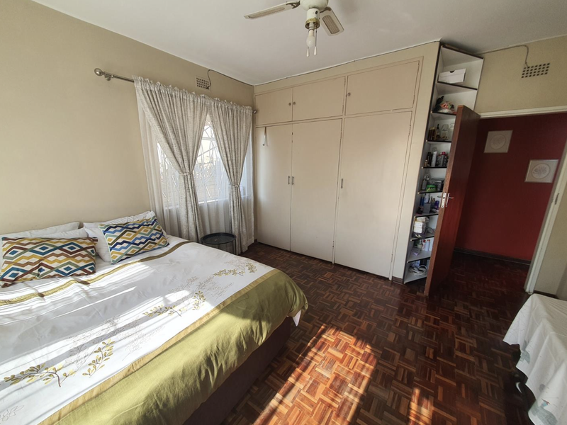 A bedroom featuring classic parquet flooring, extensive built-in cupboards with integrated shelving, and a ceiling fan, offering a functional and traditional layout.