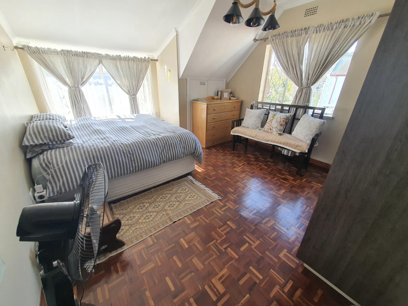 A spacious bedroom featuring classic parquet flooring, a sloped ceiling, and large windows that provide ample natural light.