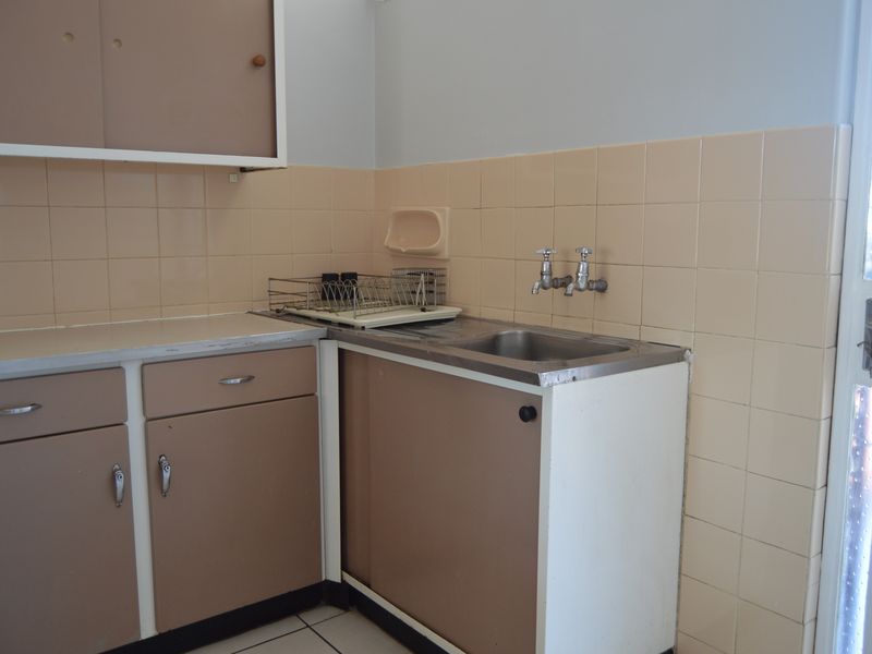 A functional laundry area featuring a stainless steel sink, dual taps, tiled splashback, and built-in cabinetry with laminate countertops.