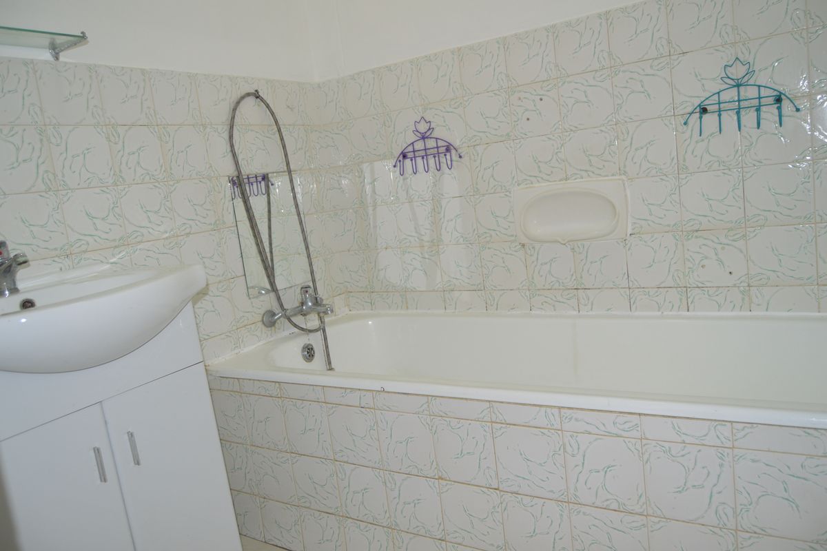 A dated bathroom featuring a standard bathtub, vanity basin, and patterned wall tiling, offering potential for a modern renovation.