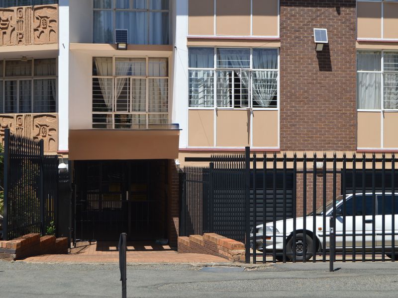Front elevation of an apartment building featuring brick and painted facade, secure metal perimeter fencing, and security bars on windows.