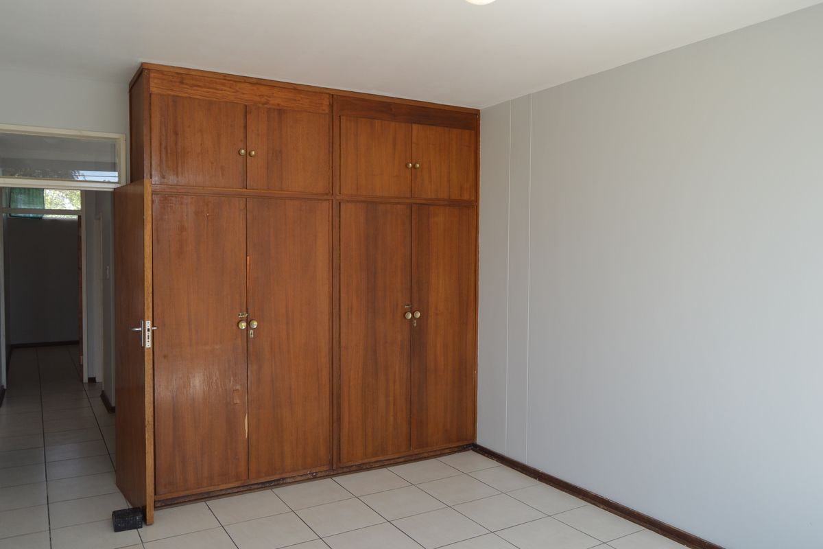 A bedroom featuring built-in wooden cupboards and tiled flooring, offering a clean, neutral space ready for personalization.