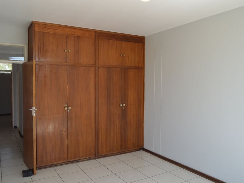 A bedroom featuring built-in wooden cupboards and tiled flooring, offering a clean, neutral space ready for personalization.