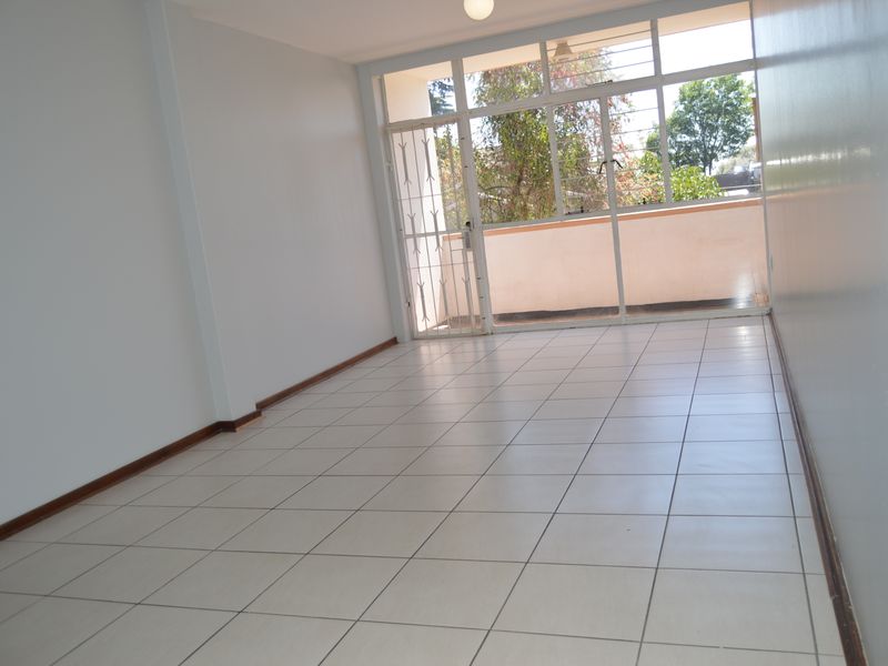 An empty, well-lit living area featuring neutral tiled flooring and a large glass sliding door providing access to an outdoor balcony.