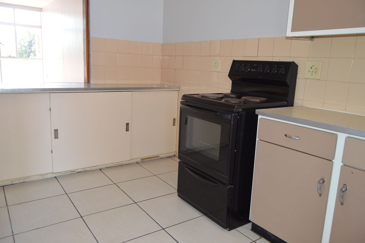 A functional kitchen featuring tiled flooring, a tiled splashback, built-in cabinetry, and a freestanding stove, offering a blank canvas for modern renovation.
