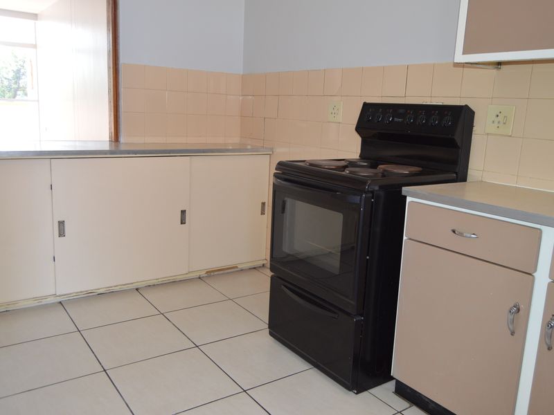 A functional kitchen featuring tiled flooring, a tiled splashback, built-in cabinetry, and a freestanding stove, offering a blank canvas for modern renovation.