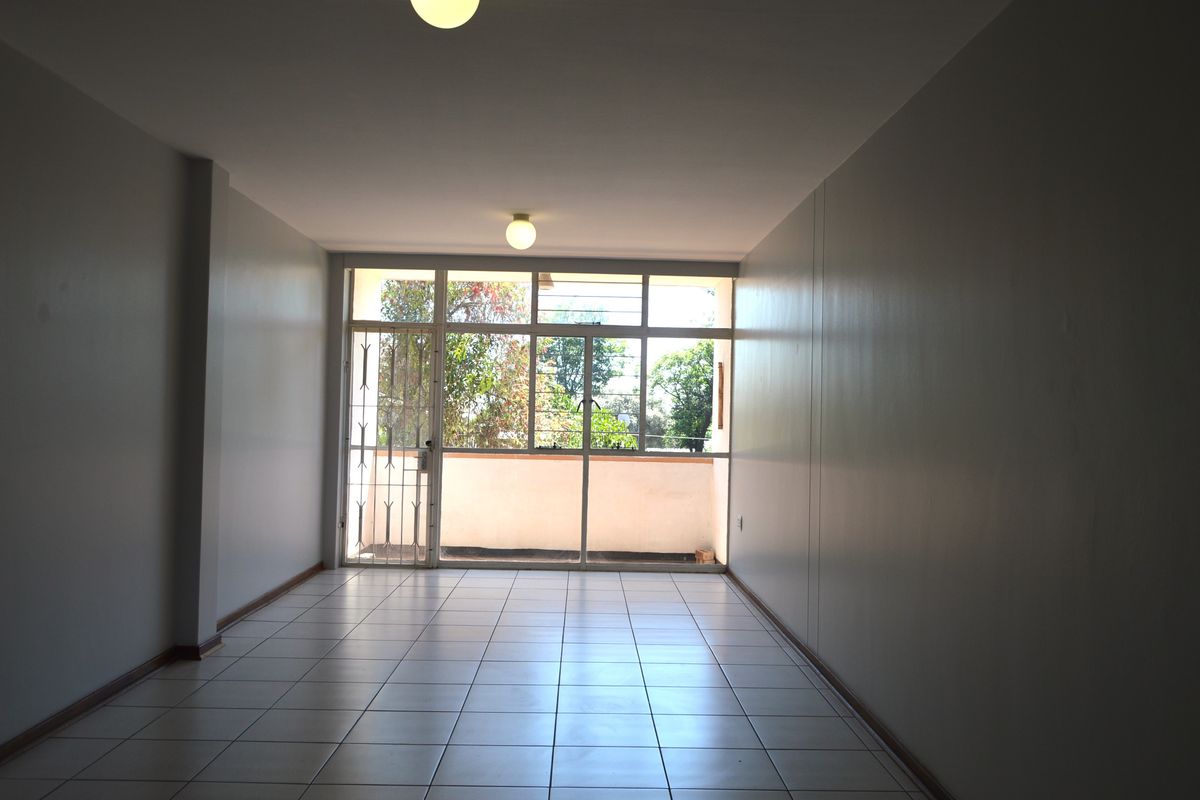 A spacious, empty living area featuring neutral tiled flooring and a large glass sliding door providing access to an outdoor balcony.