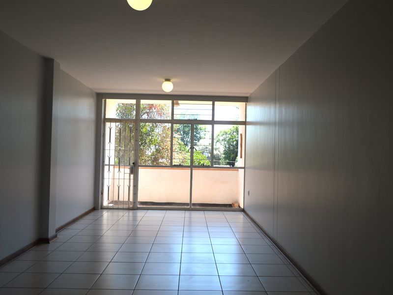 A spacious, empty living area featuring neutral tiled flooring and a large glass sliding door providing access to an outdoor balcony.