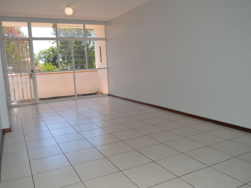 A bright, empty living area featuring neutral tiled flooring and a large glass sliding door providing access to an outdoor balcony space.
