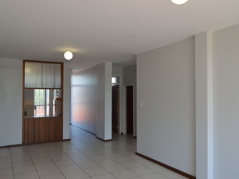An open-plan living area featuring neutral walls, tiled flooring, and a built-in wooden serving hatch connecting to the kitchen space.