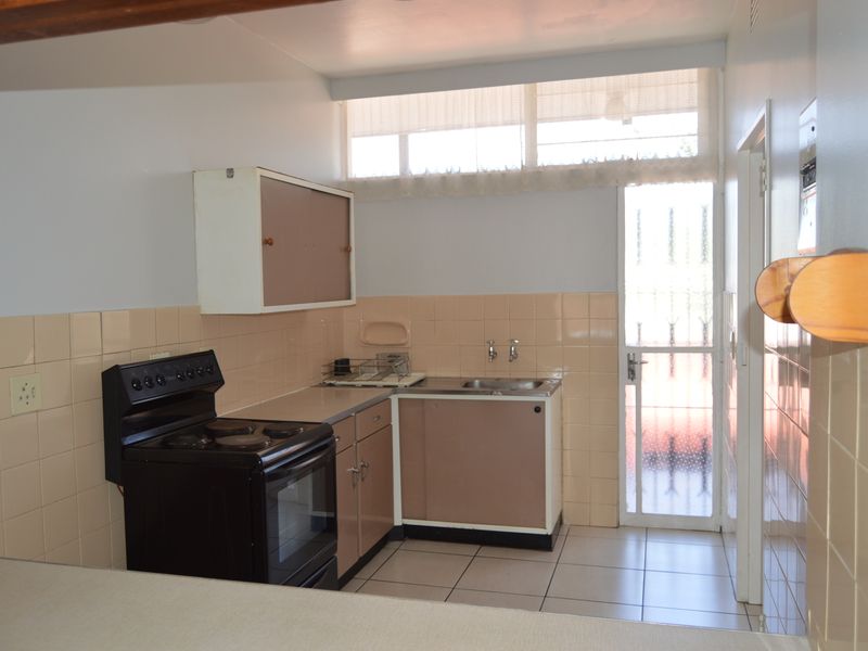 A functional kitchen featuring tiled splashbacks, built-in cabinetry, a stainless steel sink, and a freestanding stove, with direct access to an exterior area.