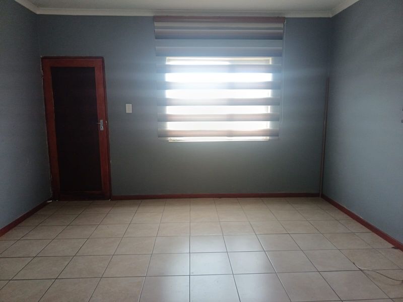 An empty bedroom featuring tiled flooring, neutral grey walls, and a window with fitted blinds.