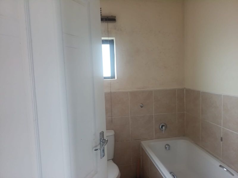 A functional bathroom featuring a bathtub, toilet, and tiled wall finishes, currently in need of cosmetic updates and maintenance.