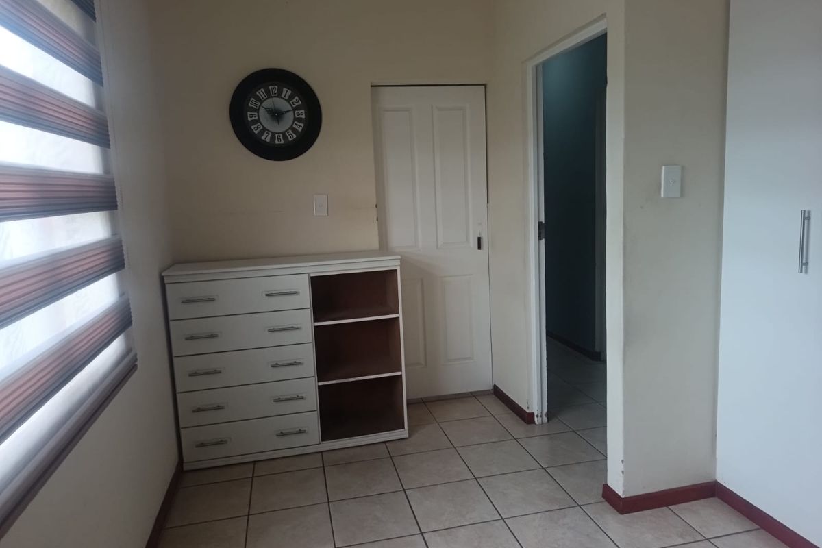 A bedroom featuring tiled flooring, a built-in cupboard, and a window with blinds. The room includes a built-in storage unit with missing drawer fronts.