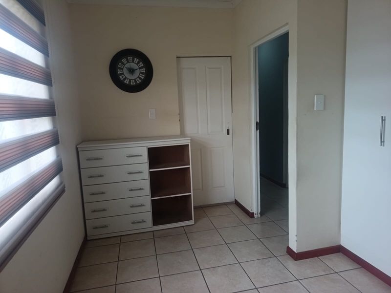 A bedroom featuring tiled flooring, a built-in cupboard, and a window with blinds. The room includes a built-in storage unit with missing drawer fronts.