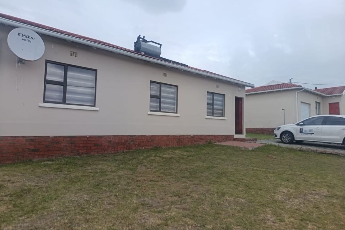 Rear view of a single-story residential house featuring a brick plinth, aluminium window frames, and a roof-mounted solar water heater.