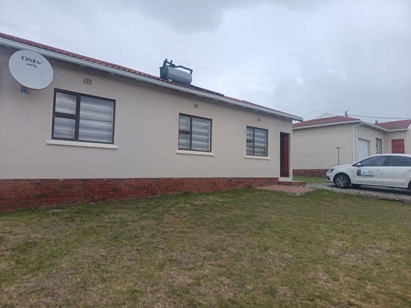 Rear view of a single-story residential house featuring a brick plinth, aluminium window frames, and a roof-mounted solar water heater.