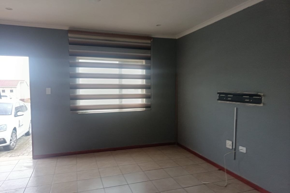 An empty living room featuring tiled flooring, neutral grey walls, and a wall-mounted TV bracket, offering a blank canvas for personalization.