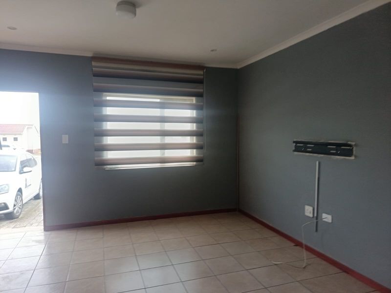 An empty living room featuring tiled flooring, neutral grey walls, and a wall-mounted TV bracket, offering a blank canvas for personalization.