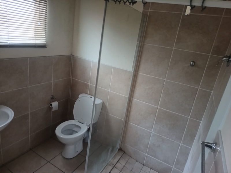 A functional bathroom featuring a shower enclosure, toilet, and basin with neutral wall and floor tiling.