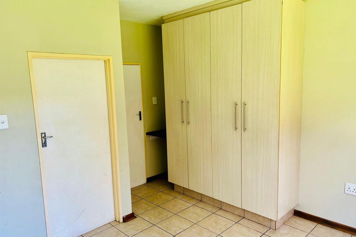 A functional bedroom featuring light-toned built-in cupboards and neutral tiled flooring, offering a clean and versatile space ready for personalization.