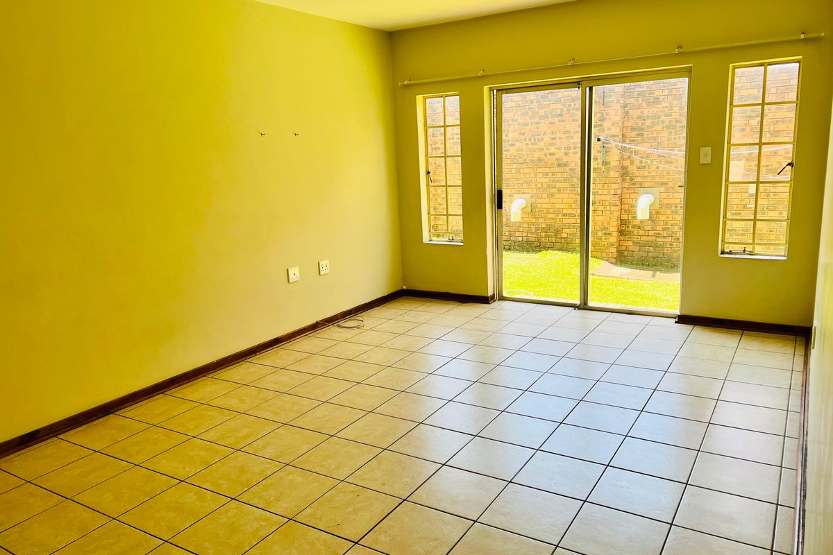 An empty living room featuring ceramic floor tiles, large sliding glass doors leading to the exterior, and natural light through side windows.