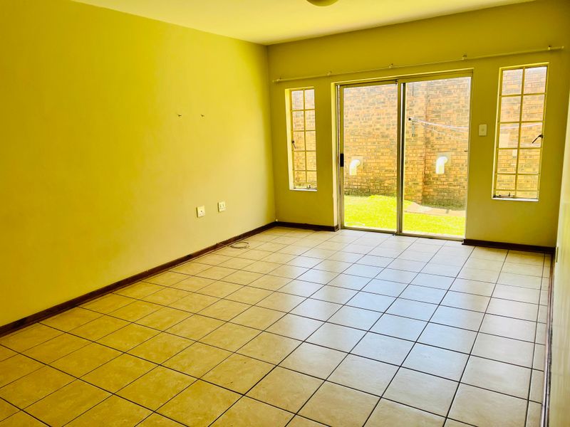 An empty living room featuring ceramic floor tiles, large sliding glass doors leading to the exterior, and natural light through side windows.