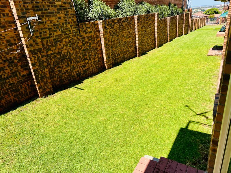 A well-maintained private garden area featuring a neat lawn and secure brick boundary wall with electric fencing.