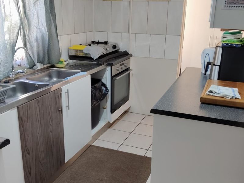 Functional kitchen featuring tiled flooring, a double basin sink, built-in oven, hob, and a mix of white and wood-look cabinetry with tiled splashbacks.