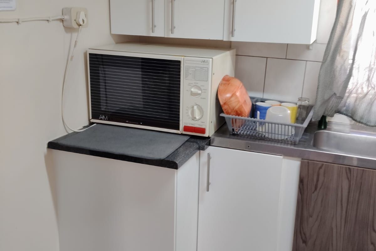 A compact kitchen area featuring white cabinetry, laminate countertops, a stainless steel sink, and tiled flooring with a tiled backsplash.