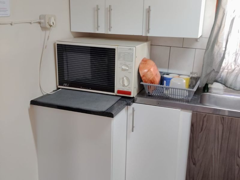 A compact kitchen area featuring white cabinetry, laminate countertops, a stainless steel sink, and tiled flooring with a tiled backsplash.