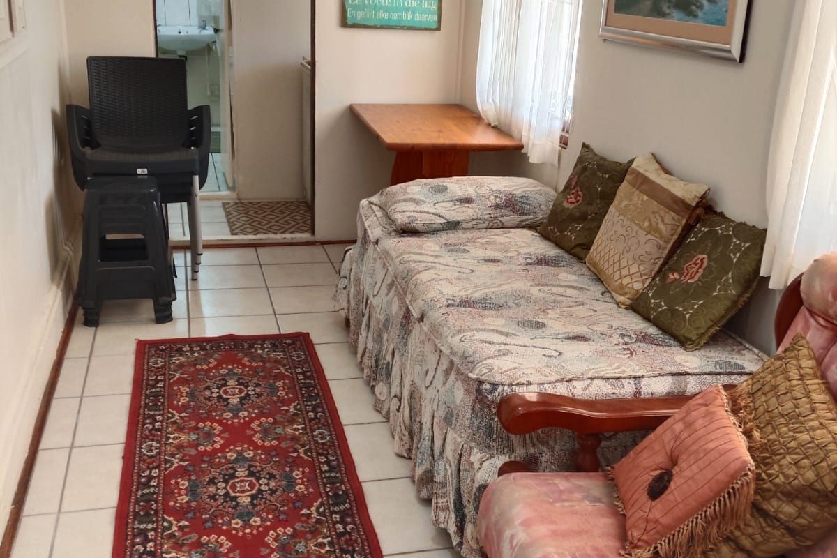 A living area featuring tiled flooring and window blinds, with an adjacent view into a bathroom space.