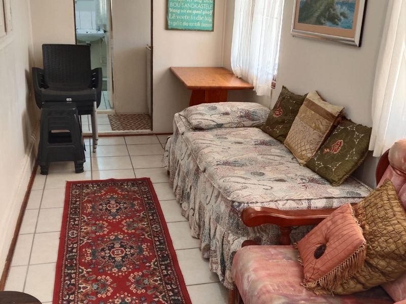 A living area featuring tiled flooring and window blinds, with an adjacent view into a bathroom space.
