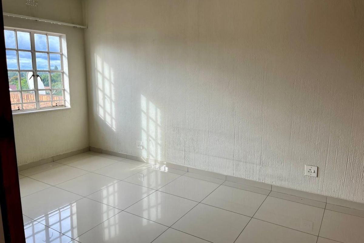 A bright, empty bedroom featuring neutral tiled flooring, textured walls, and a window with security bars, offering a clean canvas for personalization.