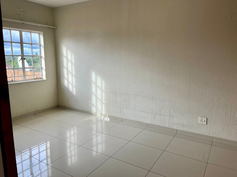 A bright, empty bedroom featuring neutral tiled flooring, textured walls, and a window with security bars, offering a clean canvas for personalization.
