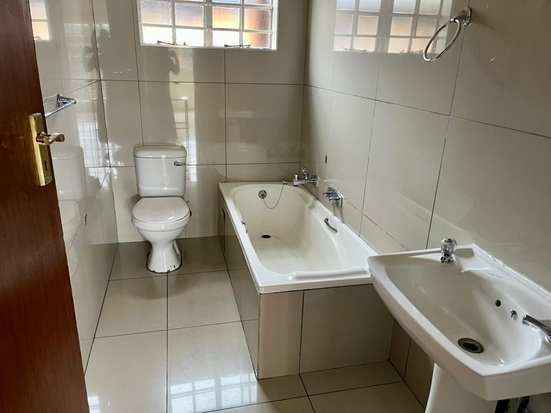 A functional bathroom featuring a bathtub, pedestal basin, and toilet with neutral wall and floor tiling.