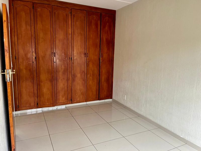 An empty bedroom featuring tiled flooring and extensive built-in wooden cupboards, offering a blank canvas for potential interior design updates.