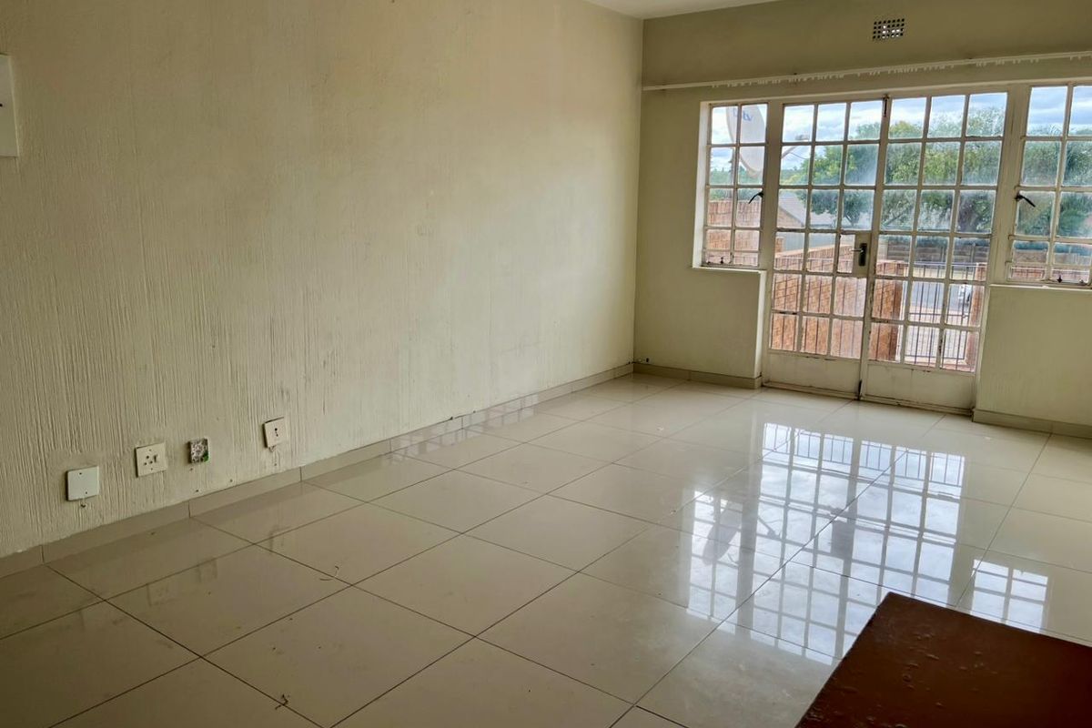 An empty living room featuring tiled flooring, large windows, and a glass-paneled door leading to the exterior.