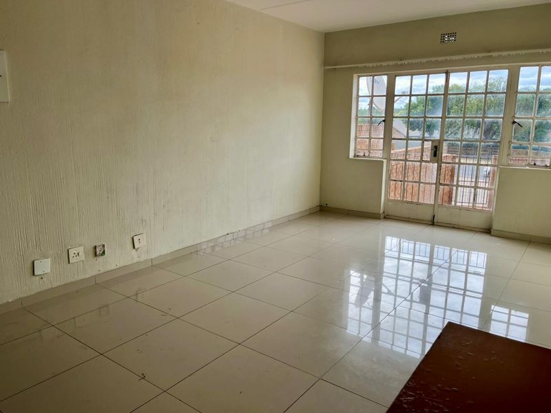 An empty living room featuring tiled flooring, large windows, and a glass-paneled door leading to the exterior.