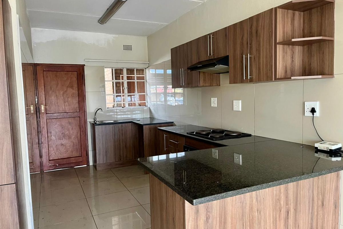 Modern kitchen featuring wood-finish cabinetry, granite countertops, an electric hob, and tiled flooring, offering a functional and clean workspace.